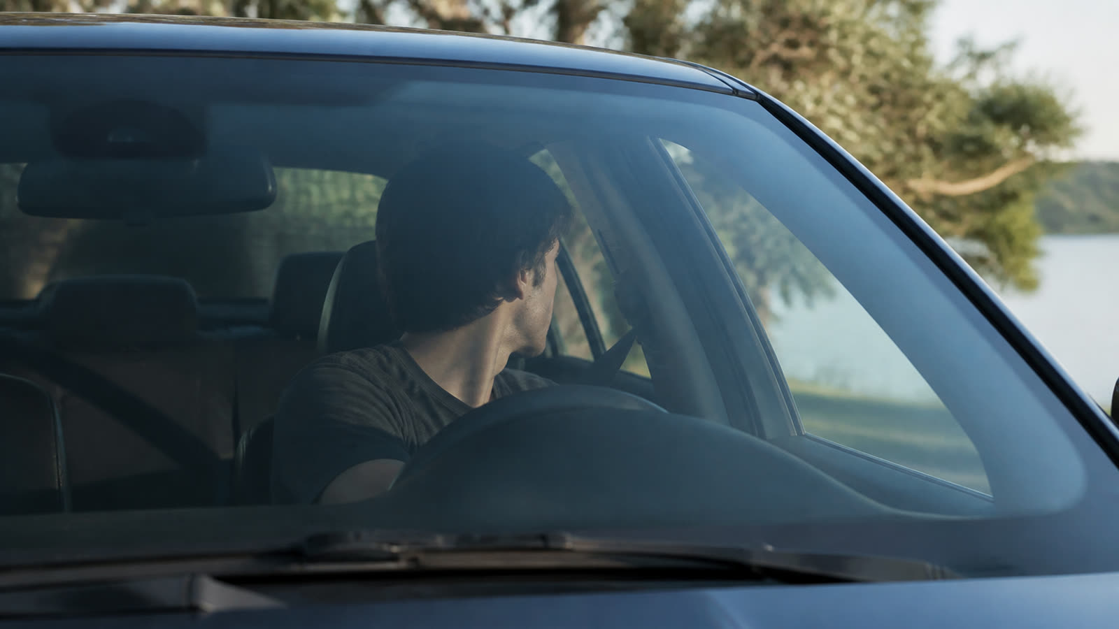 A driver sitting in a parked car, seen through the windshield