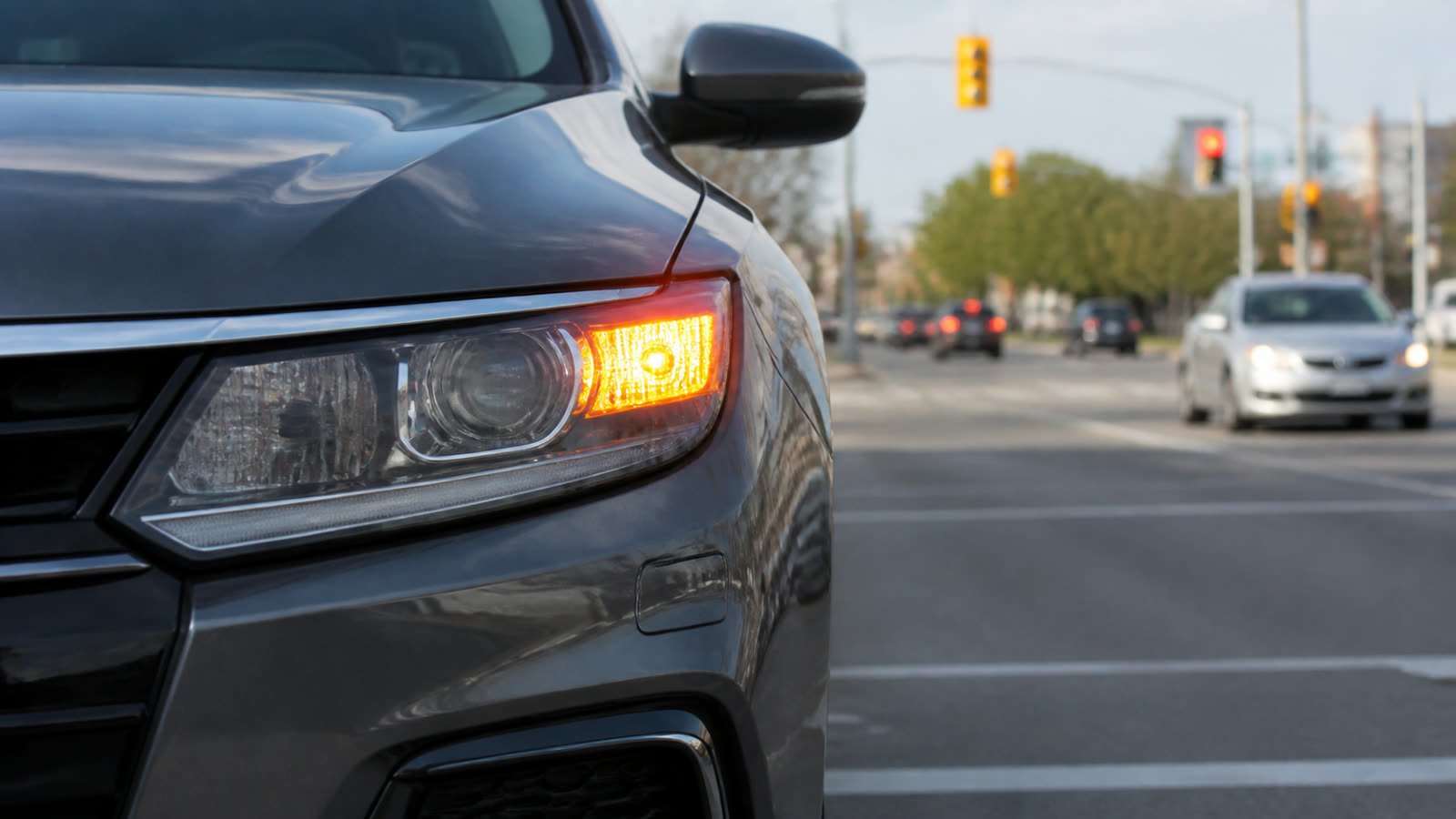 The front corner of a car with its turn signal lit at an intersection